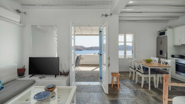 A modern interior with a TV, dining area, kitchen, and a balcony with a view.