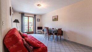 A room with a red sofa, a dining table with chairs, a TV, and a window with curtains. - Apartment 'Résidence Du Parc' with Balcony (Thônes)