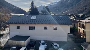 A building with a flat roof, multiple windows, and a parking area with several cars. - Apartment 'Résidence Du Parc' with Balcony (Thônes)