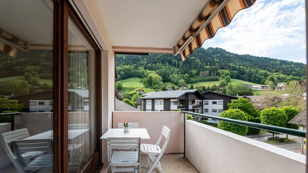 A balcony with a table and chairs, a view of a green landscape, and a building in the background. - Apartment 'Résidence Du Parc' with Balcony (Thônes)