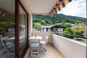 A balcony with a table and chairs, a view of a green landscape, and a building in the background.