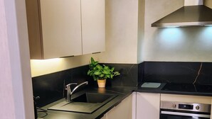 A kitchen with white cabinets, a black countertop, a stainless steel range hood, a sink, and a stove. - Apartment 'Résidence Du Parc' with Balcony (Thônes)