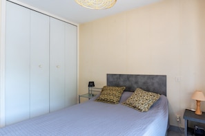 A bedroom with a bed, two pillows, a bedside table with a lamp, and a wardrobe.