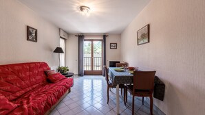 A room with a red sofa, a dining table with chairs, a lamp, and a ceiling light fixture. - Apartment 'Résidence Du Parc' with Balcony (Thônes)
