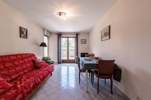 A room with a red sofa, a dining table with chairs, a lamp, and a ceiling light fixture.