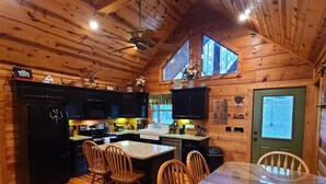Interior de una cabaña de madera con cocina, comedor y un amplio ventanal.