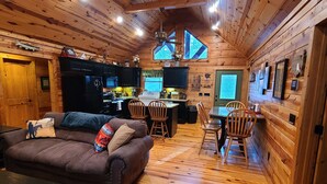Interior acogedor de una cabaña con techo de madera, comedor, sofá y cocina.