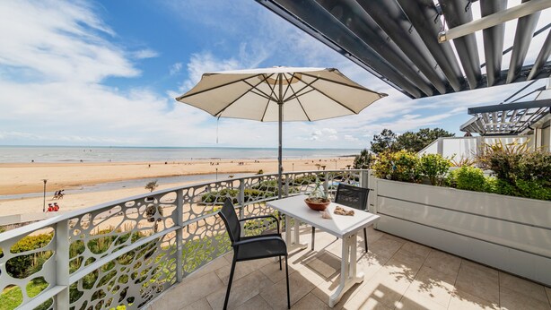 A balcony with a table and chair, overlooking a beach. - Apartment 'Résidence Le Rêve' with Shared Pool, Wi-Fi and Air Conditioning (La Tranche-sur-Mer)