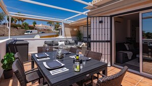 Un patio al aire libre con una mesa de comedor, mobiliario de mimbre y una puerta corrediza de vidrio que da a una zona de estar interior.