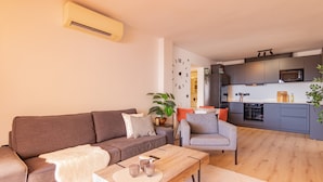 Una sala de estar moderna con sofá, sillón, mesa de centro y una cocina al fondo.