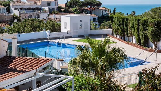 Una piscina en la azotea con vistas al mar, rodeada de vegetación y edificios.