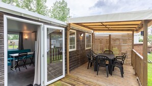 A covered patio with a table and chairs, a sliding glass door leading to an interior space, and a wooden deck. - Mobile Home 'Mobil-home' with Shared Pool and Private Terrace (Angles)