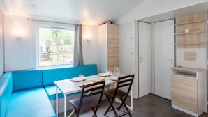 A modern room with a dining table, chairs, a bench, a window with curtains, and built-in shelves. - Mobile Home 'Mobil-home' with Shared Pool and Private Terrace (Angles)