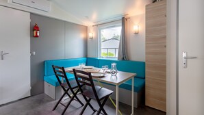 A compact room with a table, chairs, a bench, a window, and a door. - Mobile Home 'Mobil-home' with Shared Pool and Private Terrace (Angles)