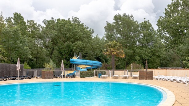 A swimming pool with a water slide, lounge chairs, and a wooden fence. - Mobile Home 'Mobil-home' with Shared Pool and Private Terrace (Angles)