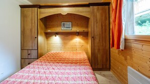 A wooden-paneled room with a bed, a shelf with a picture, and a window with curtains. - Apartment 'Village Gaulois-appt 48r' with Mountain View and Balcony (Saint-François-Longchamp)