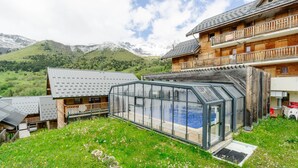 A chalet with a glass-enclosed pool, wooden balconies, and a mountainous backdrop. - Apartment 'Village Gaulois-appt 48r' with Mountain View and Balcony (Saint-François-Longchamp)