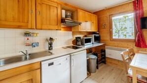 A compact kitchen with wooden cabinets, a dishwasher, a microwave, and a window with a view of trees. - Apartment 'Village Gaulois-appt 48r' with Mountain View and Balcony (Saint-François-Longchamp)