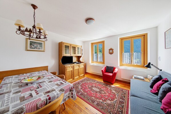 A room with a dining table, a sofa, a red chair, a chandelier, wooden cabinets, and a window with a view.