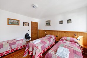 A room with two beds, a wooden headboard, a wooden door, and a wall-mounted light fixture.