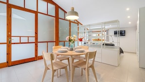 A modern dining area with a round table, chairs, a vase with flowers, and a kitchen area with a TV.