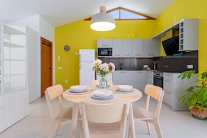 Una cocina moderna con una pared amarilla, armarios blancos y un comedor con una mesa preparada para cuatro comensales.
