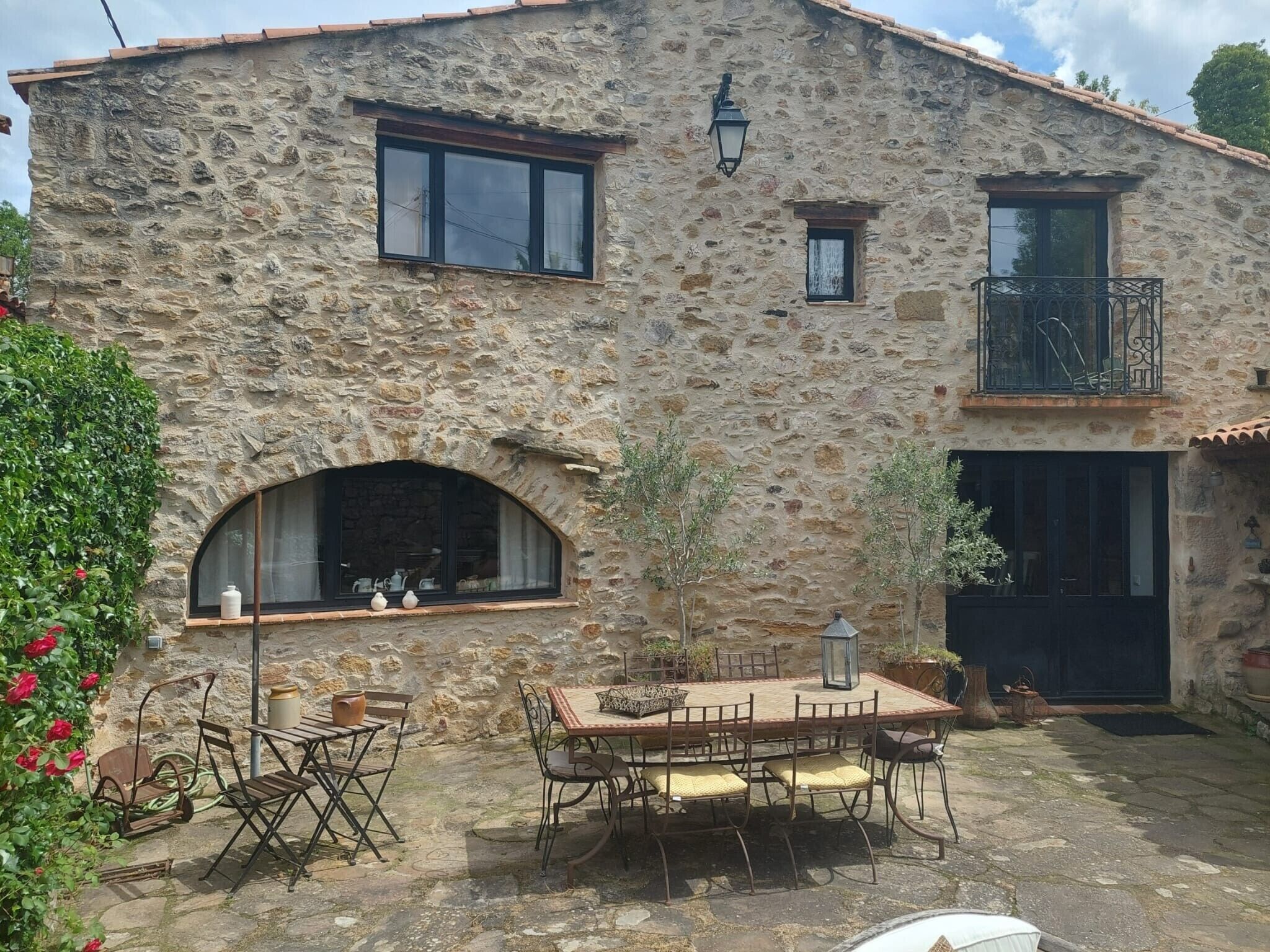 A stone building with a balcony, a dining area with outdoor furniture, and a window with a view.