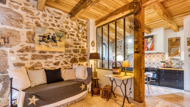 Una stanza accogliente con parete in pietra, soffitto in legno, un divano decorato con una stella, un tavolo con una lampada e un angolo cottura con pensili e un fornello.
