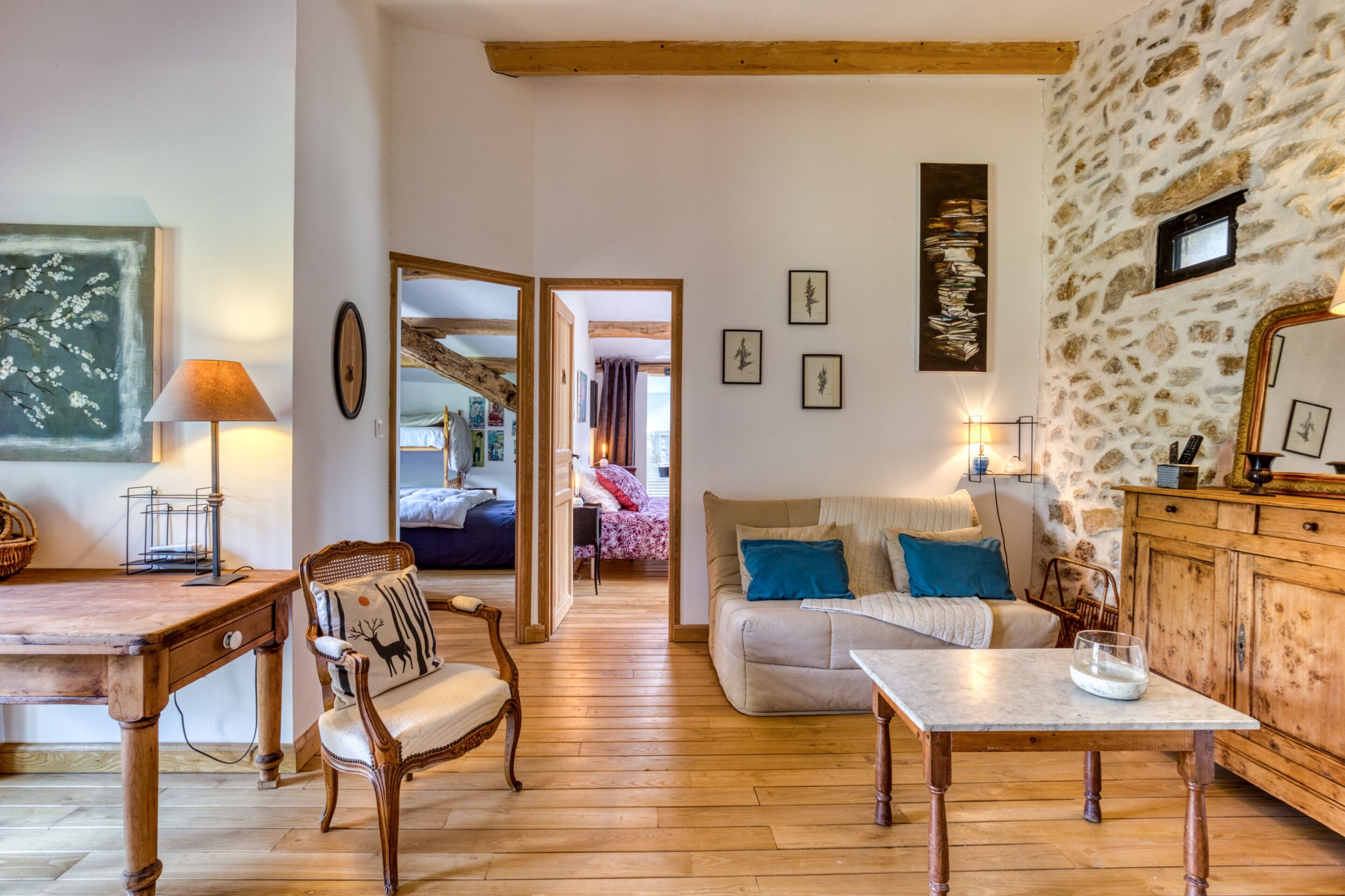 A cozy room with a wooden floor, a sofa, a table, and a chair. There is a mirror, a lamp, and a picture frame on the wall.