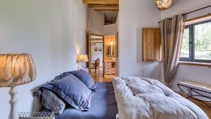 Una camera da letto con un letto, una lampada, una finestra con tende e un trave in legno al soffitto.