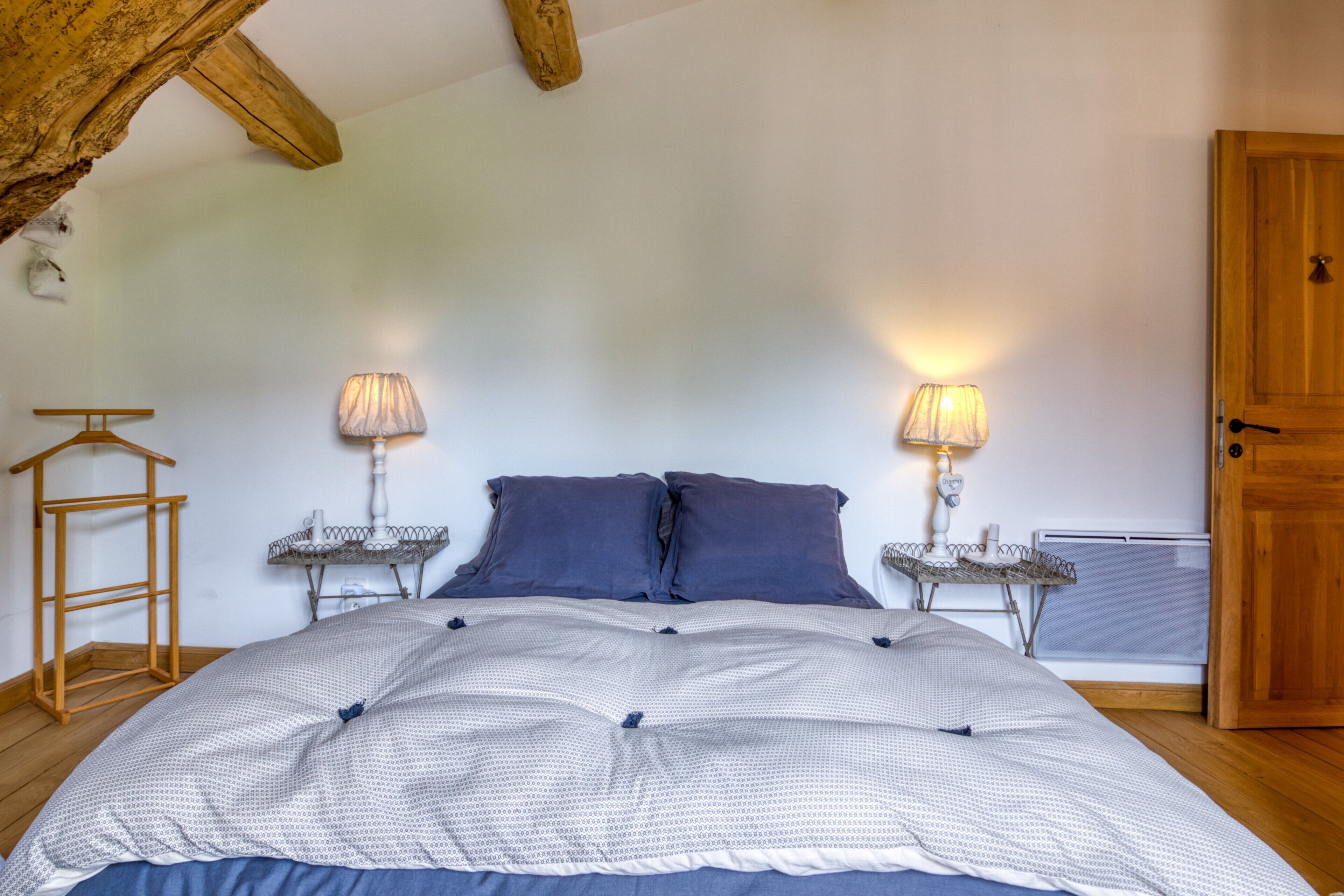 A bedroom with a bed, two bedside tables with lamps, a wooden hanger, and a door.