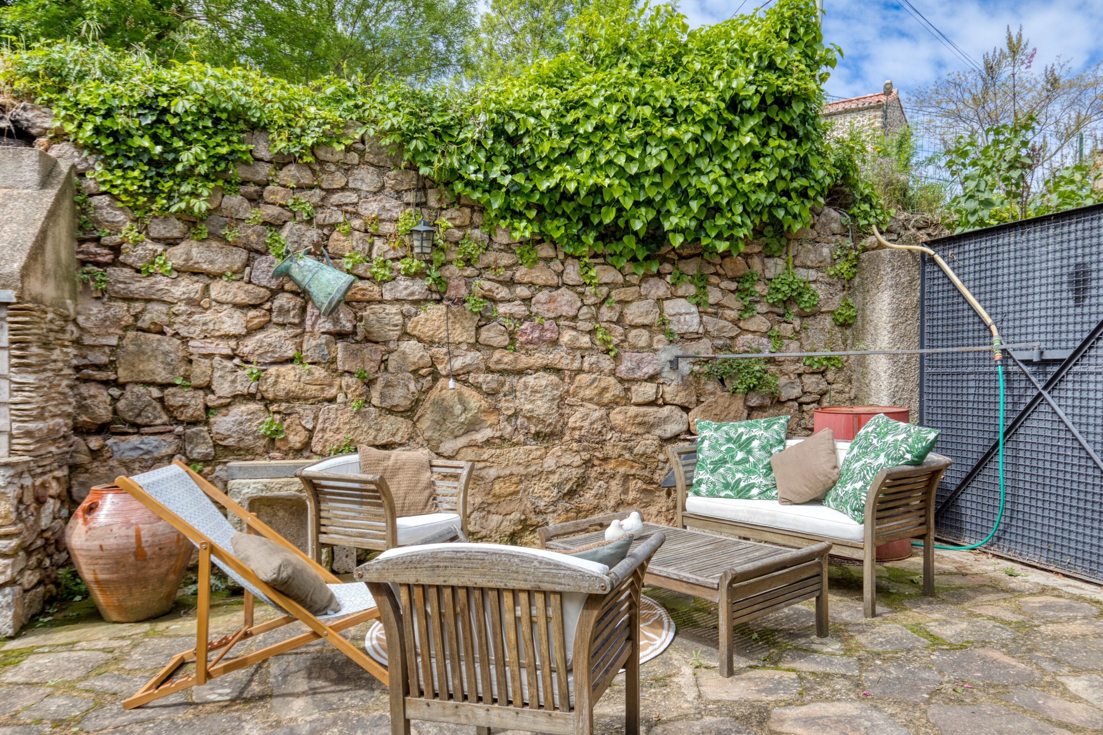 Un mur de pierre agrémenté de verdure, des meubles d’extérieur et un portail en métal.