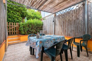 Un patio cubierto con una mesa lista para comer, rodeado de sillas y una valla de madera con plantas.