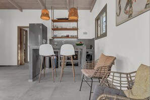 Et moderne køkken med indbygget køleskab, spiseområde med to hvide stole, en fletsofa og en hængende lampe.