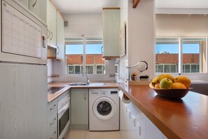 Une petite cuisine équipée d’un lave-linge, d’un évier et d’un saladier rempli de fruits posé sur le plan de travail.