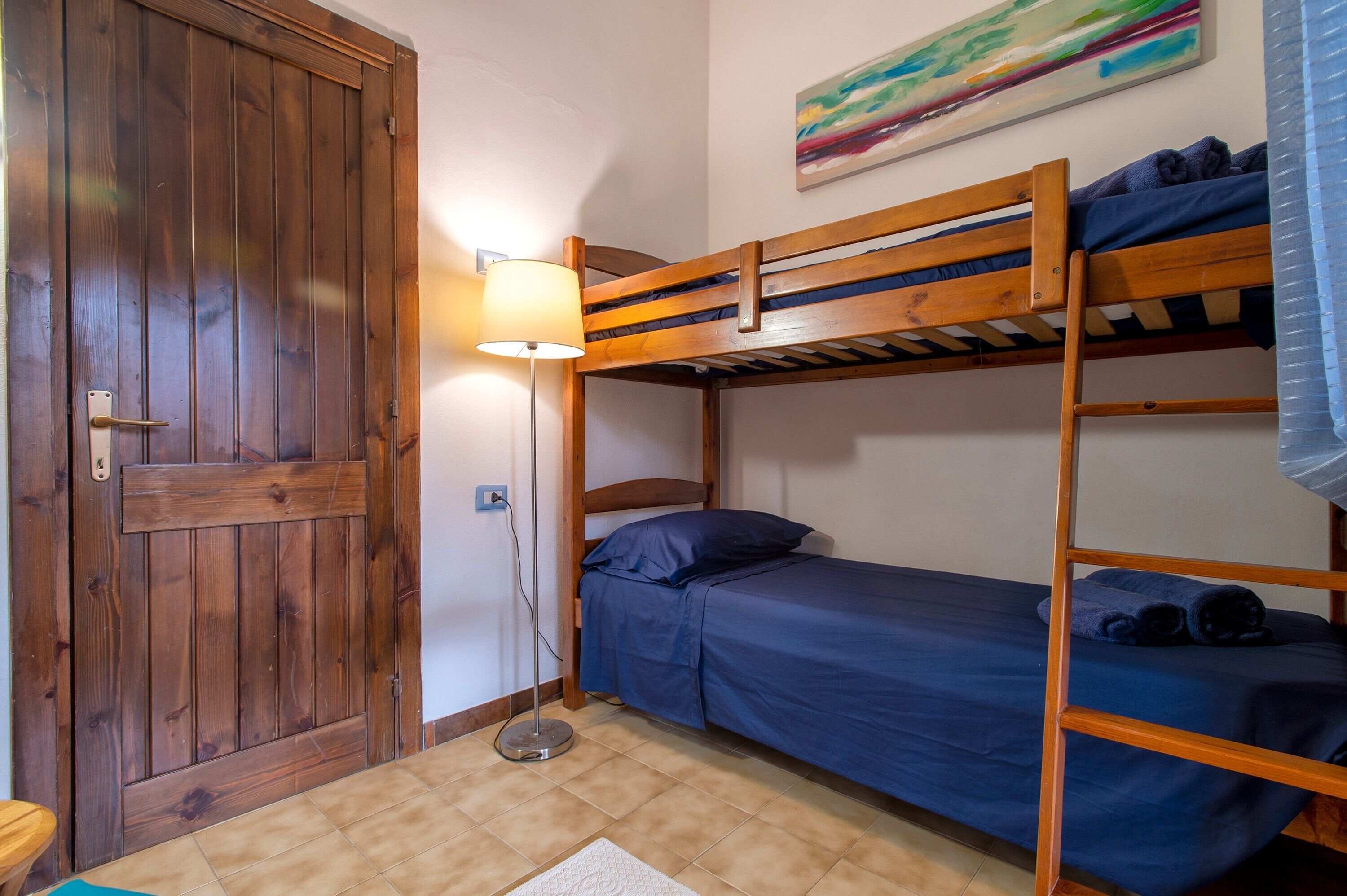 A bunk bed room with a wooden door, a floor lamp, and a painting on the wall.