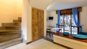 A staircase leading to a wooden door, a dining area with a table and chairs, and a view through a window with blue curtains. - Holiday Home 'Casetta Al Mare' with Wi-Fi – A/C in Bedroom (Valledoria)