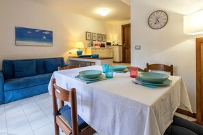 Un comedor con una mesa dispuesta para cuatro, un sofá azul y una cocina al fondo.