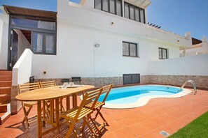 A swimming pool with a tiled deck, a wooden table with chairs, and a white building with windows and a door. - Vacation Home 'Lin House' with Private Pool, Private Terrace and Wi-Fi (Corralejo)
