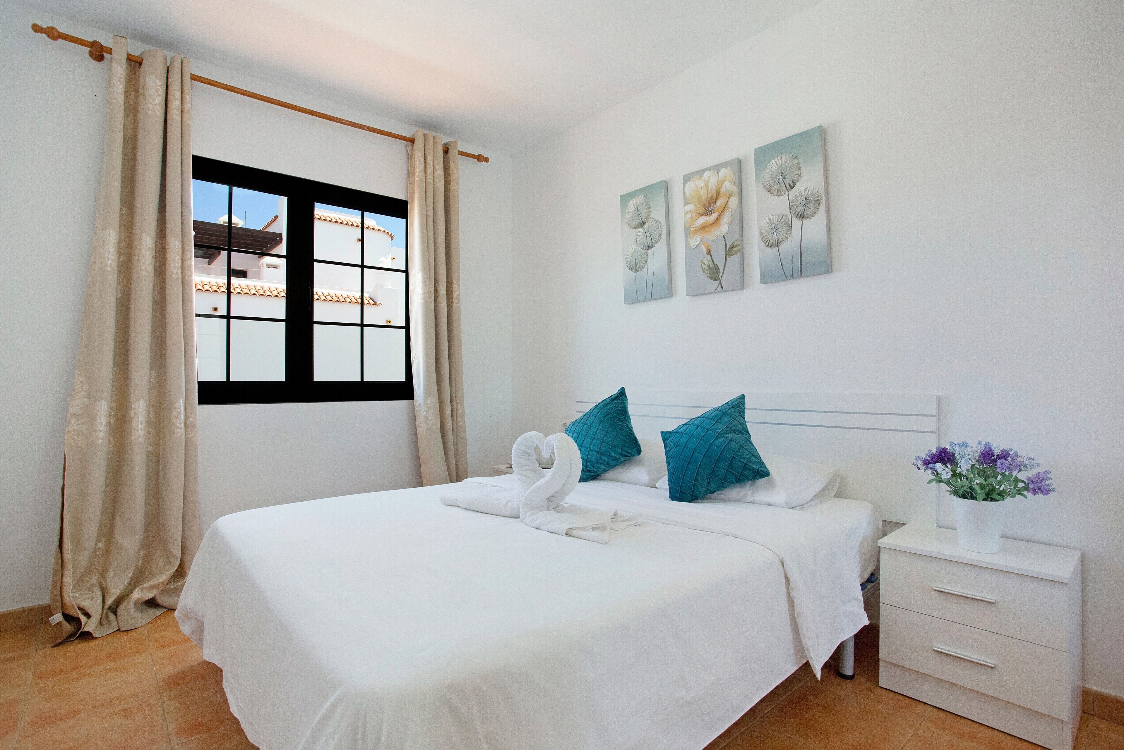 Ein Hotelzimmer mit Bett, Fenster, Nachttisch und Wandbildern.