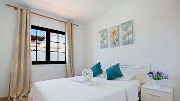Ein Hotelzimmer mit Bett, Fenster, Nachttisch und Wandbildern.