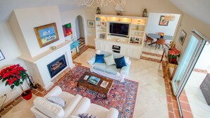 Uma sala de estar ampla com lareira, uma televisão grande e um candelabro.