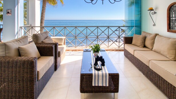 Varanda mobiliada com móveis de vime, uma mesa com uma planta e vista para o mar.