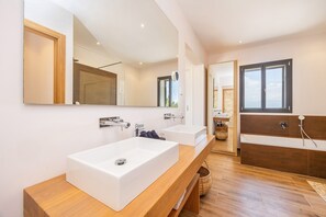 A modern bathroom with two white sinks, a large mirror, a bathtub, and a wooden vanity. - Villa 'Viduleto' with Mountain View, Private Pool and Wi-Fi (Felanitx)
