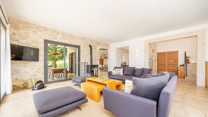 Ein modernes Wohnzimmer mit Steinwand, einem Flachbildfernseher, einer Couch, einem Couchtisch und einem Essbereich mit Tisch und Stühlen.
