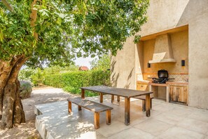 An outdoor patio with a wooden table and benches, a tree, and a kitchen area with a stove and cabinets. - Villa 'Viduleto' with Mountain View, Private Pool and Wi-Fi (Felanitx)