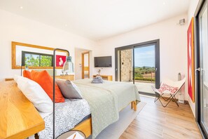 A modern bedroom with a bed, a TV, a balcony, and a chair. - Villa 'Viduleto' with Mountain View, Private Pool and Wi-Fi (Felanitx)
