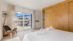 Une chambre avec un grand lit, une armoire en bois, une chaise et une vue sur l’extérieur.