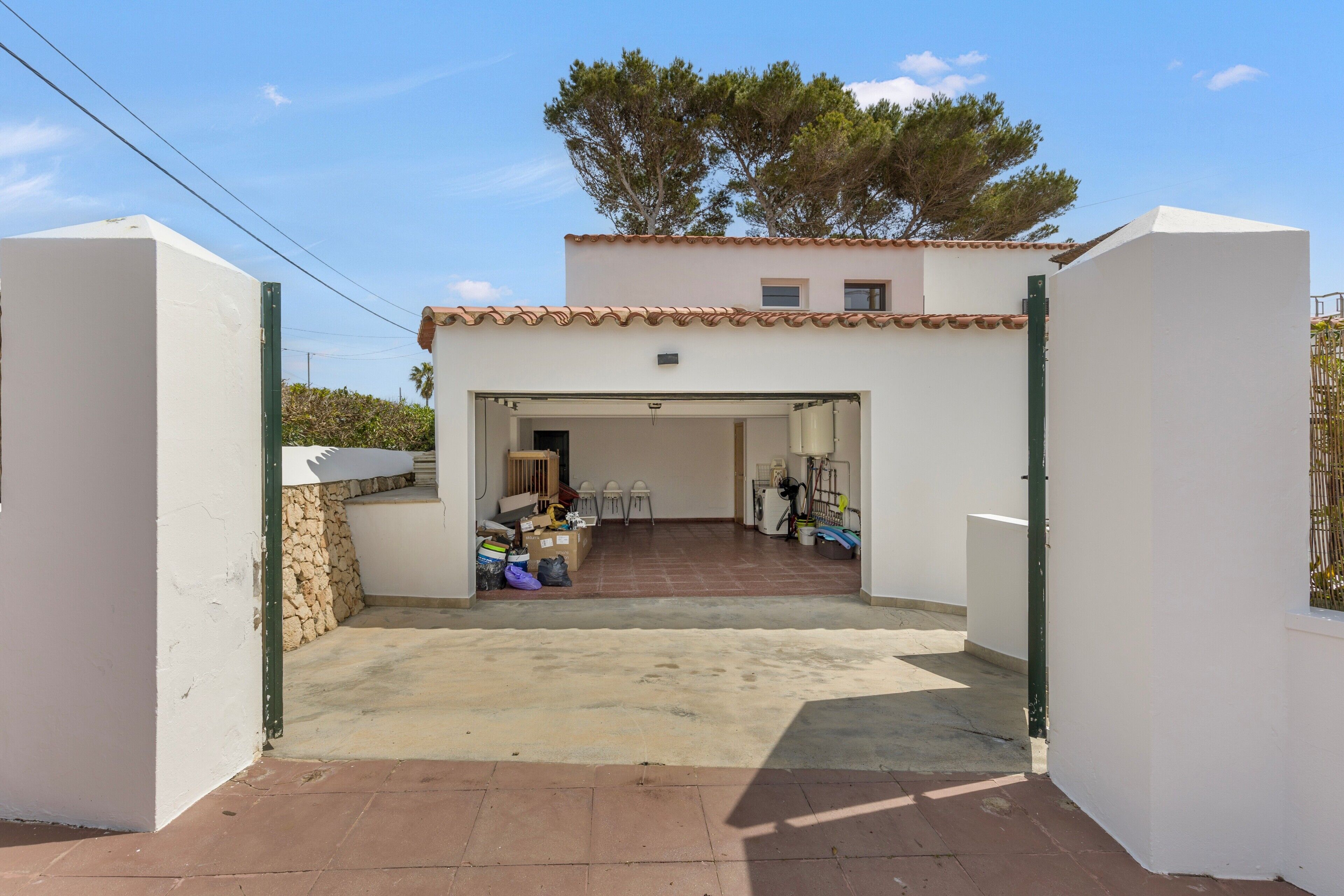 Un bâtiment blanc avec un toit en tuiles, une entrée couverte et un petit patio agrémenté de divers objets et de mobilier.