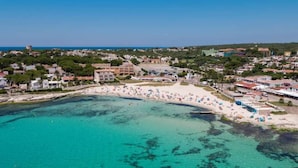 Vue aérienne d’une ville côtière avec une plage, des bâtiments et des eaux turquoise limpides.